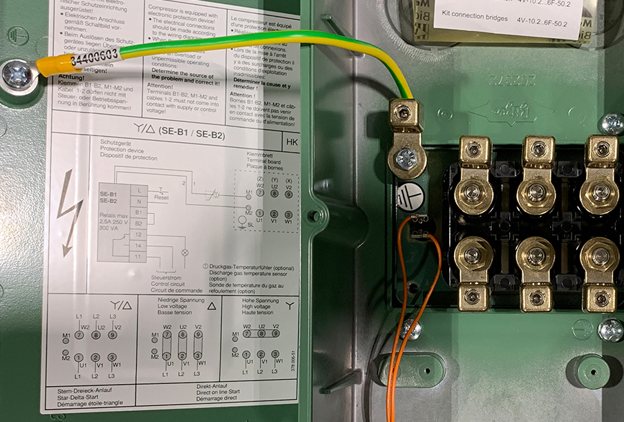 Клеммная коробка поршневого компрессора BITZER. Клейкая этикетка на крышке показывает пример правильного подключения фаз сети к контактам мотора для пуска по схеме «звезда-треугольник» и прямого пуска по схеме «треугольник» и «звезда» (слева направо).